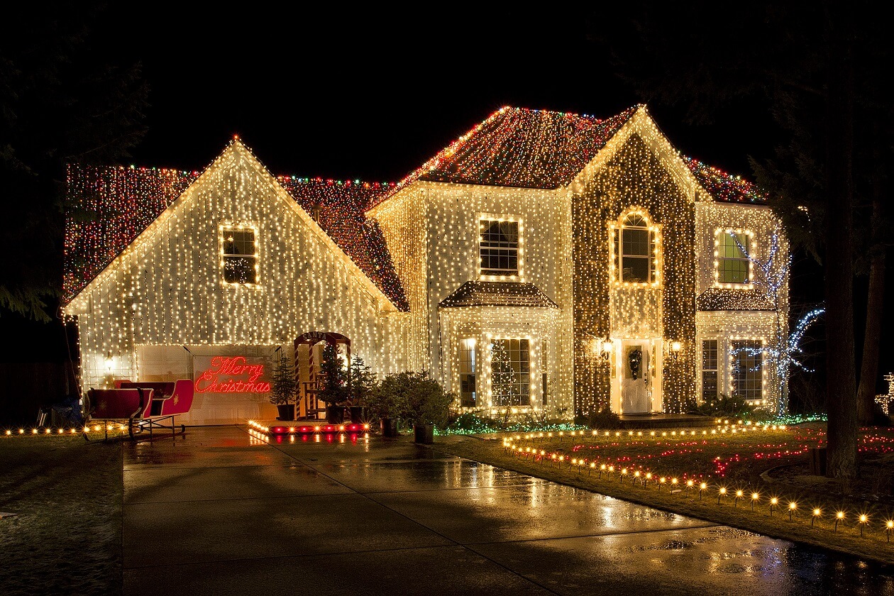 Large home covered in warm white curtain lights with multicolor roofline accents